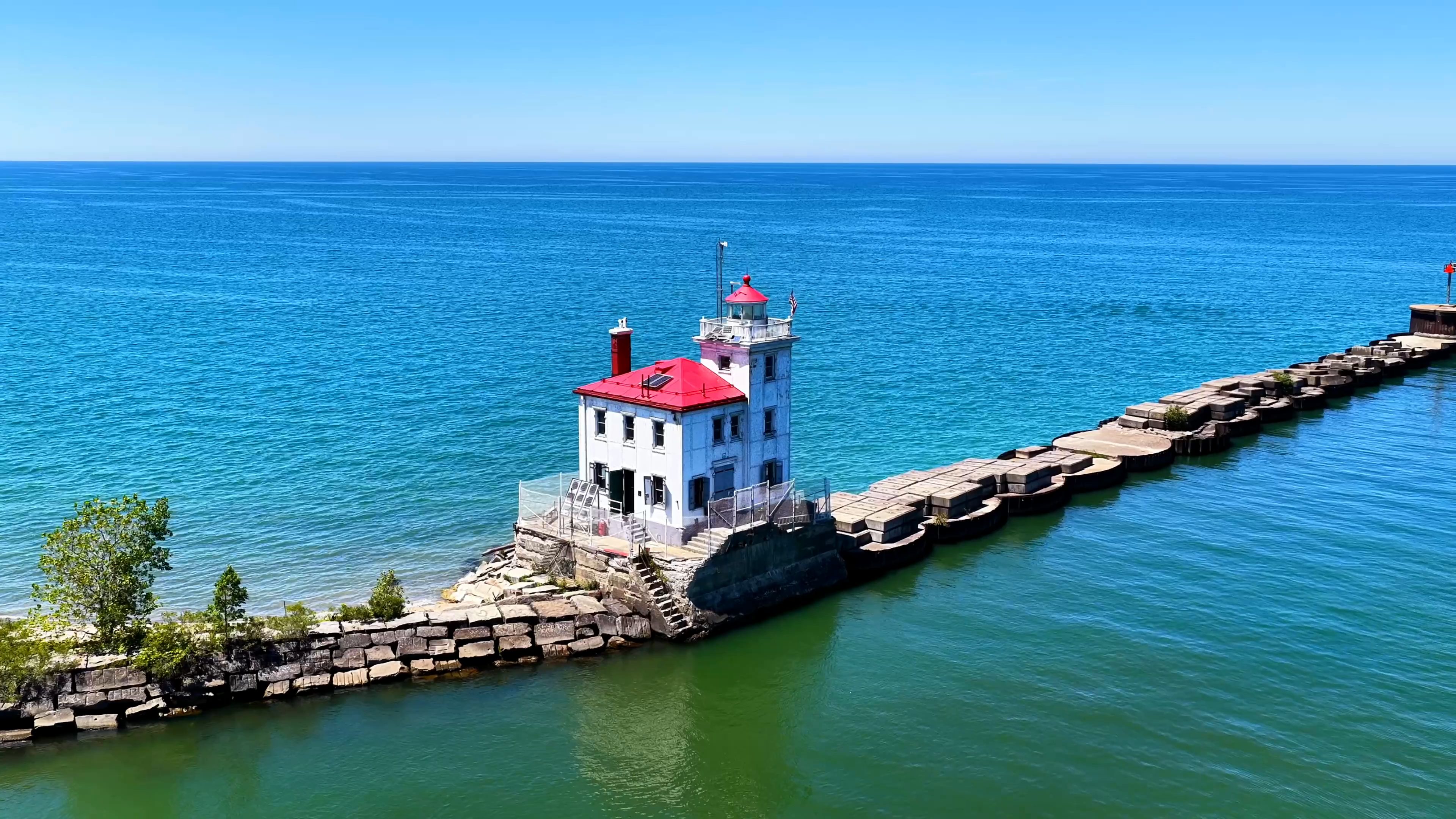 Lighthouse at the end of a stone breakwater on turquoise water, drone photo by Horizon Heights Productions.