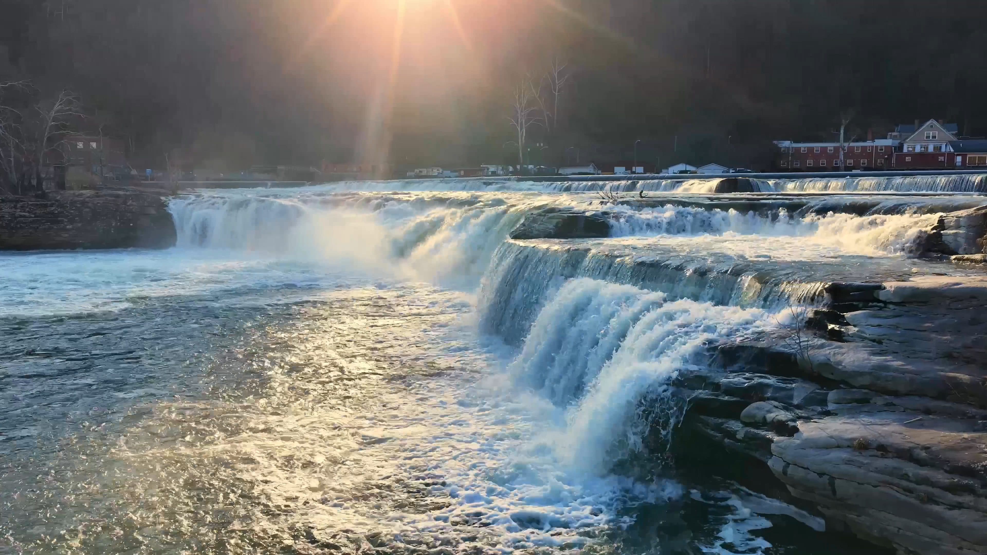 Golden backlit waterfall cascading over layered rock ledges, filmed by Horizon Heights Productions.