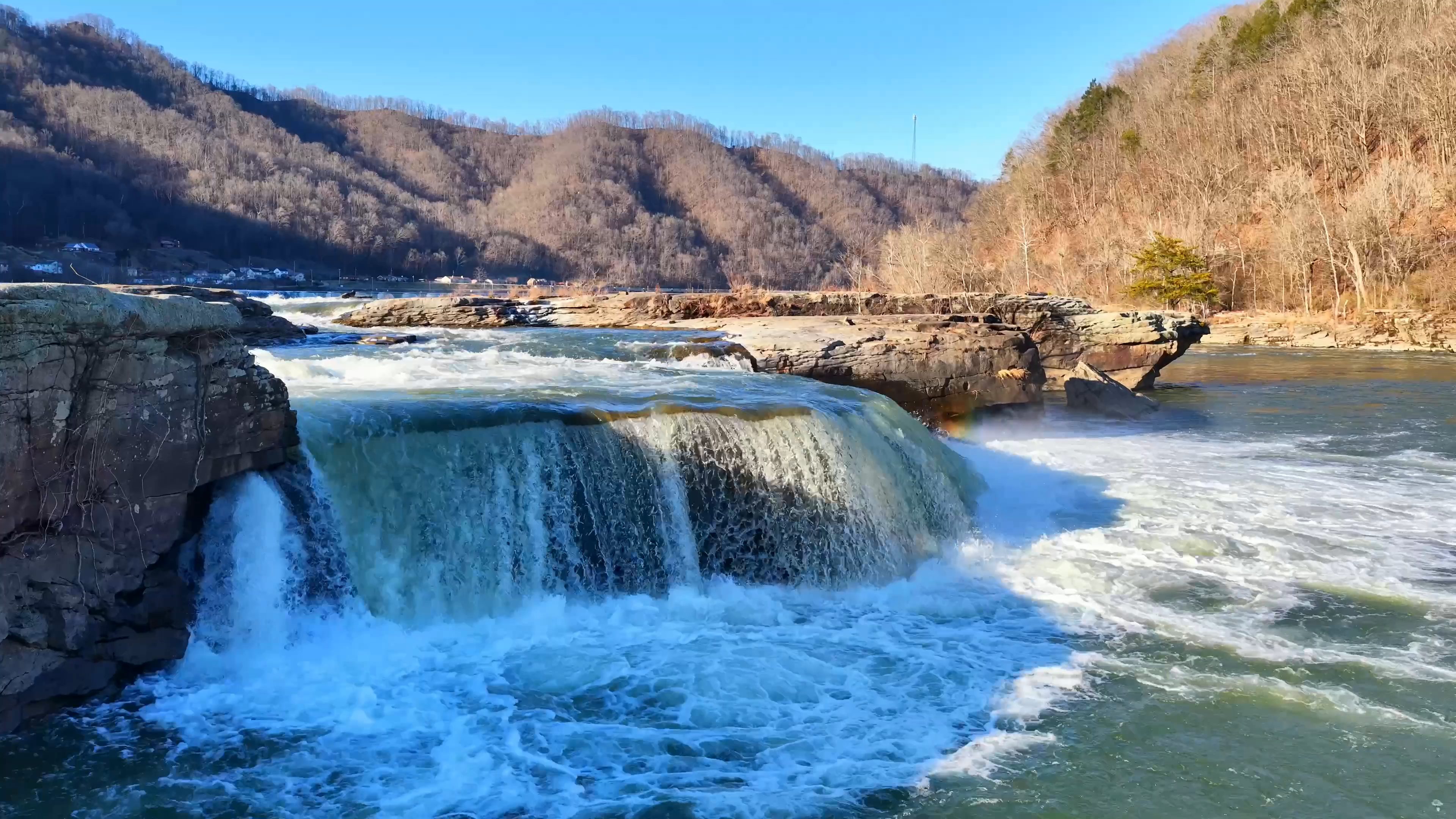 Aerial view of a wide waterfall in a sunlit Appalachian river gorge, filmed by Horizon Heights Productions.