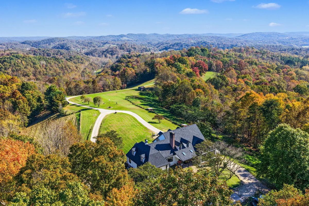 High aerial looking out from above the house over a valley of fall-color forest, ridgelines fading to blue. 469 Vincent Hill Rd, Cairo, West Virginia, shot for Whitetail Properties.